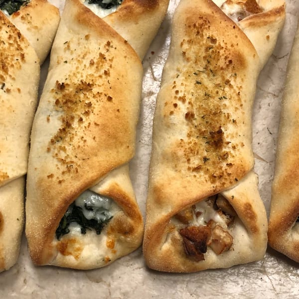 Close-up of golden-brown baked dough pockets, one filled with spinach and cheese, another with chicken.