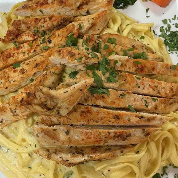 Sliced grilled chicken breast with herbs on a bed of creamy fettuccine pasta.