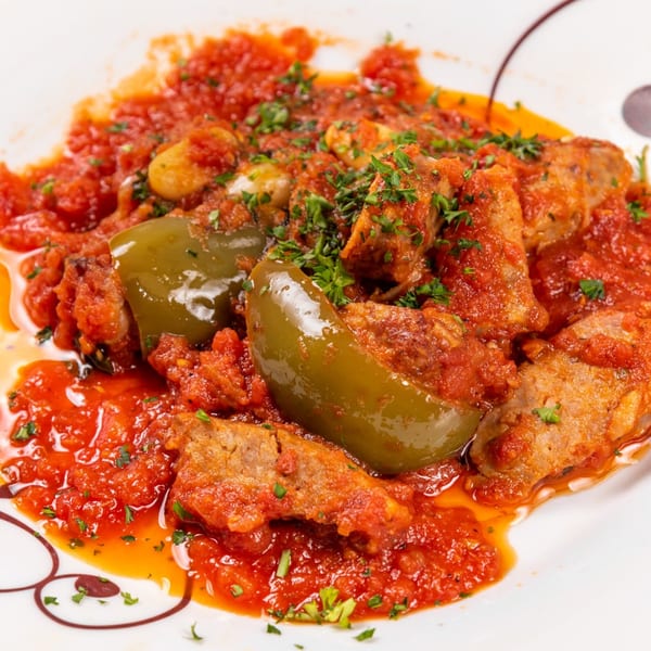 Sausage and peppers in a rich red tomato sauce, garnished with fresh parsley on a white plate.