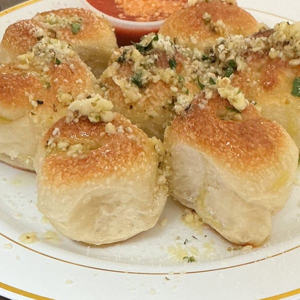 Golden-brown garlic knots topped with parmesan cheese and parsley, served with a side of marinara sauce.