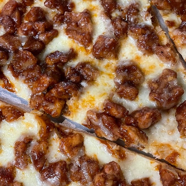 Close-up of a pizza with melted cheese and chunks of barbecue chicken, with slices cut.
