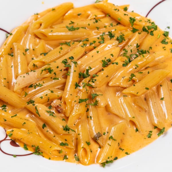 Penne pasta in a creamy orange sauce, garnished with fresh chopped parsley on a white plate.