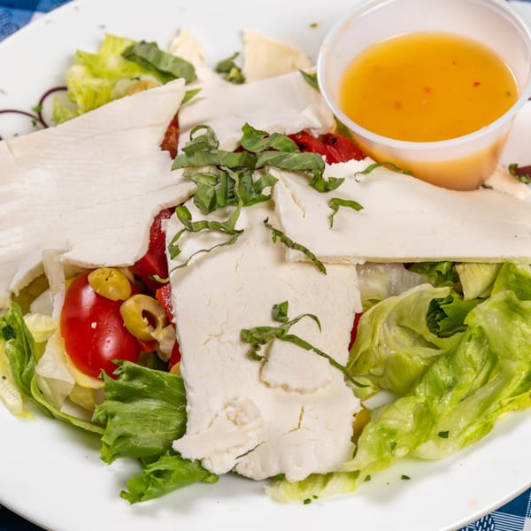 A fresh salad with lettuce, tomatoes, olives, feta cheese, basil, and a side of dressing.